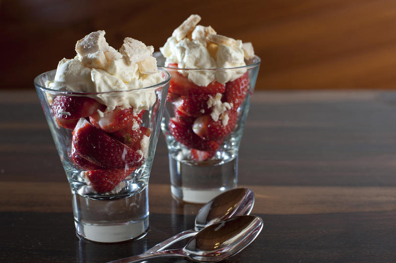 Delicious fresh ripe red strawberries and whipped cream dessert served in two sundae glasses on a wooden counter with copyspace
