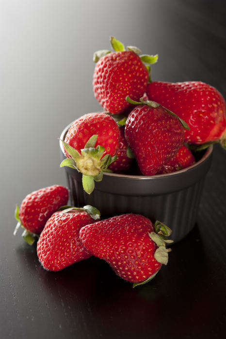 Fresh ripe red strawberries overflowing from a ceramic dish onto a dark background with side lighting