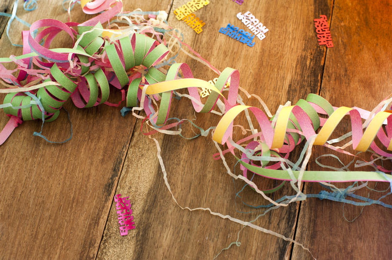 Jumble of colorful paper party streamers entwined and coiled on a wooden table with scattered multicolored Happy Birthday confetti, with copyspace