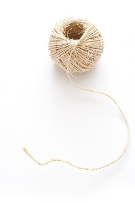 Ball of common household string or twine with the end curled outwards over a white background, high angle view
