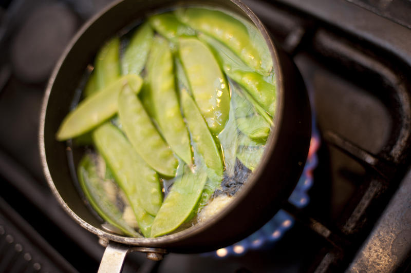 Mangetout peas boiling in a pot on a gas stove for a delicious accompaniment to a meal or vegetarian and vegan cuisine