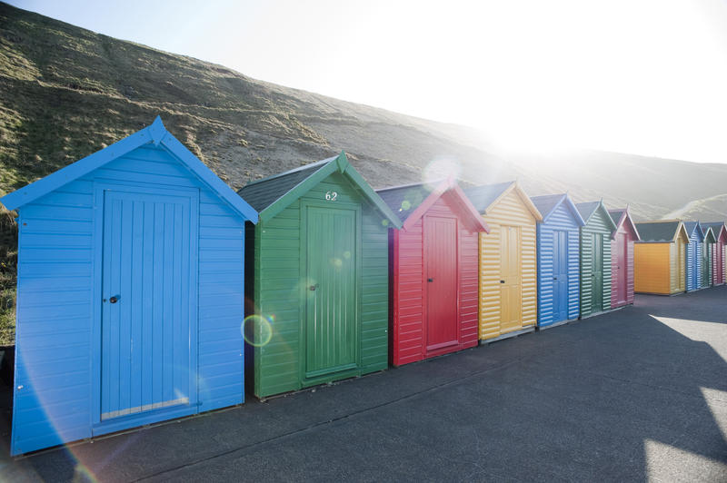 Row of brightly coloured wooden beach huts on Whitby West Cliff under a hot sun for changing when bathing