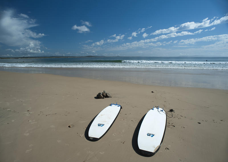 Two surfboards lying side by side on a deserted tropical beach in the summer sunshine with a calm ocean and small waves in the background