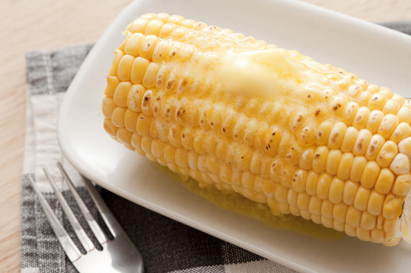 Grilled fresh sweet corn on the cob ready to eat topped with a blob of melting butter, serving on a plate