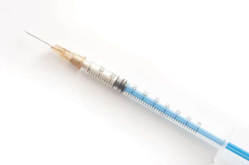 Small plastic disposable hypodermic syringe and needle for self administering drugs in a disease such as diabetes lying diagonally on white with copyspace