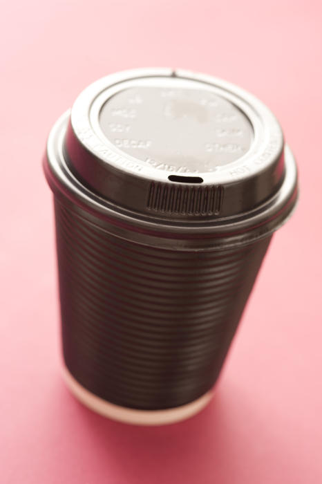 Plastic takeaway hot beverage container for coffee or cappuccino with a closed lid on a red background