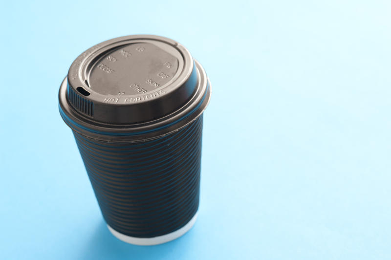Brown plastic takeaway cup with a closed lid on a blue background with copyspace