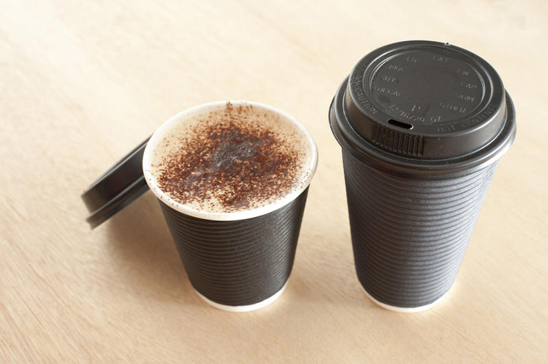 Close Up of Two Take Out Cups of Coffee on Wooden Background - High Angle View of Coffee in Paper Disposable Cups, One with Lid and One Without Showing Frothy Beverage with Cocoa Dusting