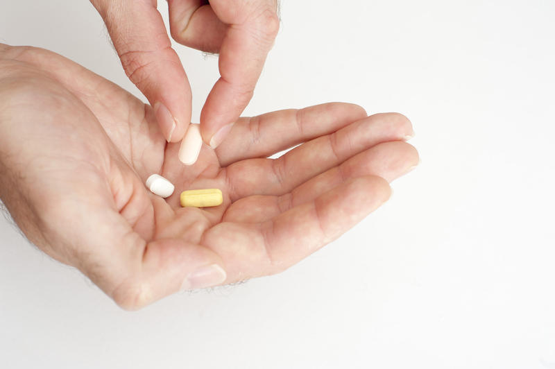 Person taking medication lifting a tablet from a cocktail of three in his hand in a healthcare concept, close up over a white background