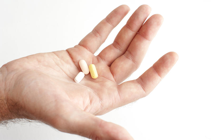 Man taking his daily medication holding out his palm containing three capsules and tablets in a healthcare and medical concept