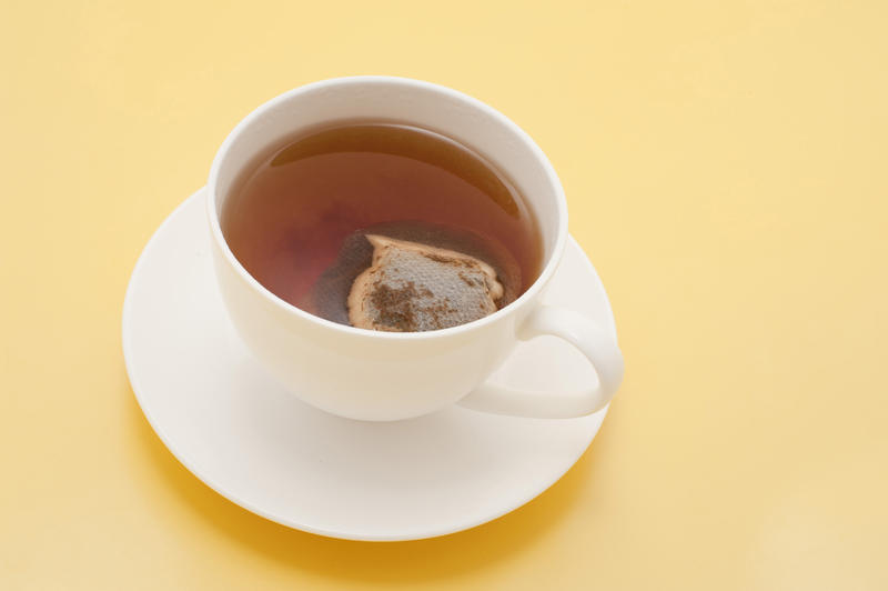 Cup of freshly brewed refreshing hot black tea served in a plain white cup and saucer for a relaxing morning tea break viewed high angle on a yellow background with copyspace