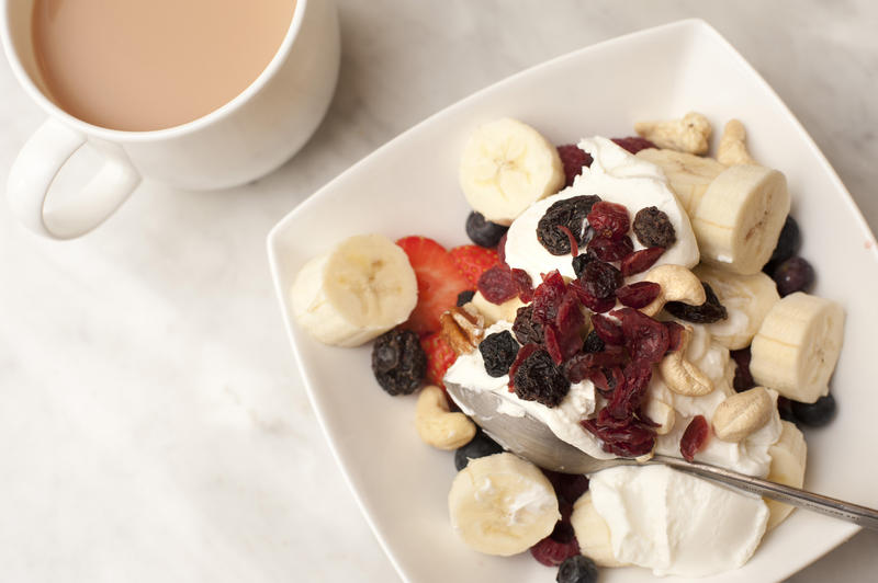 Tea and healthy breakfast cereal topped with yoghurt , raisins and sliced fresh strawberry and bananas, high angle view