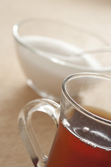 Close-up of glass of black tea and bowl of sugar