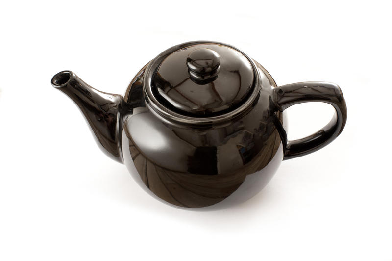 High angle view of a bulbous black ceramic glazed teapot for brewing a refreshing cup of tea on a white background