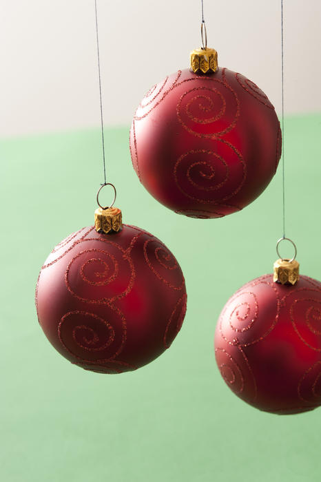Three hanging red Christmas baubles with glitter decoration over a bicolour green and white background
