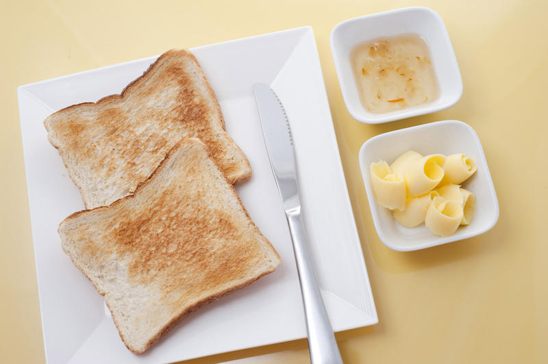 Overhead view of two slices of golden white toast with butter and marmalade on the side for a traditional breakfast