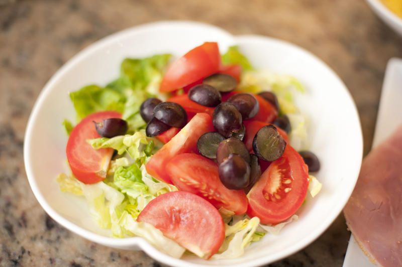 White ceramic bowl with green salad, grapes and tomatoes, high-angle close-up