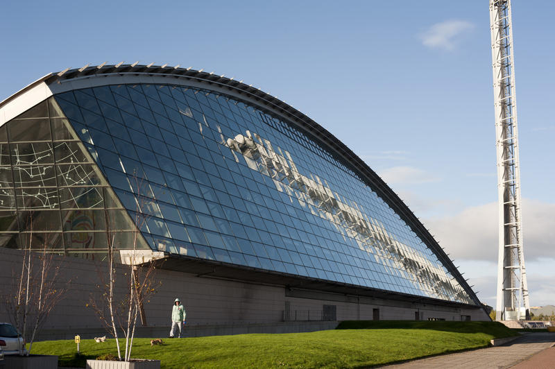 View of the curved metal exterior facade of the Glasgow Science Centre with the Glasgow Tower reflected in the titanium