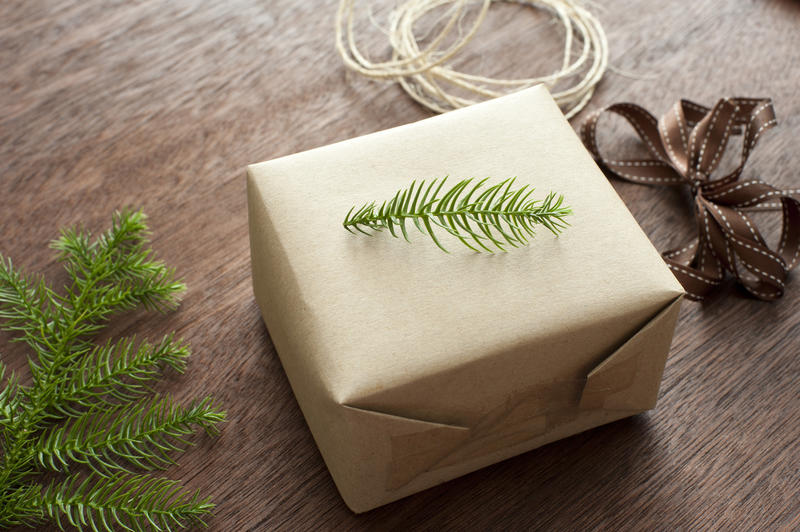 Traditional Christmas gift wrap with a small twig of fresh green pine placed on top of a wrapped gift surrounded by twine, ribbon and a pine branch