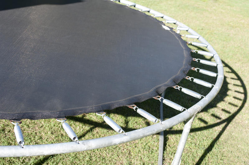 Small circular recreational trampoline with its metal frame and strong springs standing outdoors in the sunshine on the grass, close up view