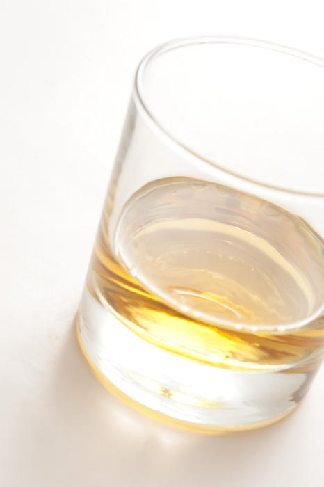 Tumbler of neat whiskey or scotch with a golden glow viewed at a tilted angle