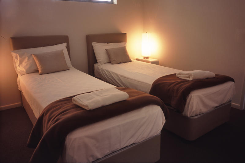 Twin beds in an illuminated bedroom with throw rugs and towels in a hotel or bed and breakfast accommodation