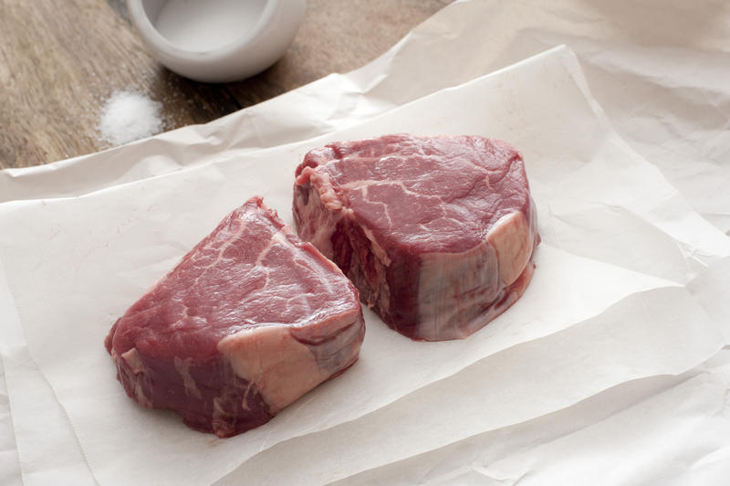 Close-up of two pieces of beefsteak on baking paper.