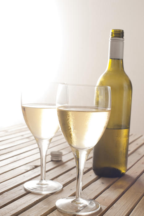 Two glasses of white wine with a half full unlabelled bottle standing on a wooden table with bright copyspace