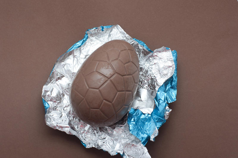 Unwrapped milk chocolate Easter egg nestling on its colourful blue and silver foil wrapper