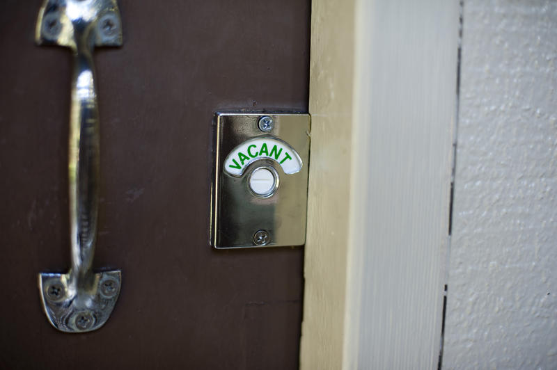 Close up Brown Wooden Toilet Door with Metal Handle and Vacant Sign