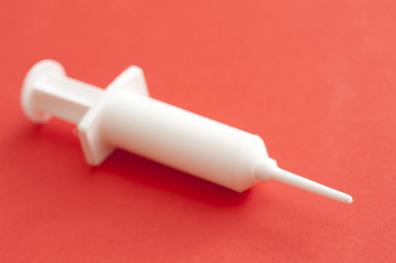 Single dose white plastic disposable vaccination syringe on a red background in a medical, travel and healthcare concept