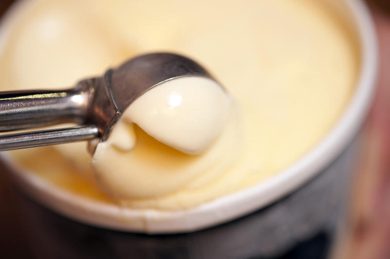 Serving a scoop of rich creamy vanilla ice cream from a small bowl with a stainless steel kitchen scoop, close up soft focus