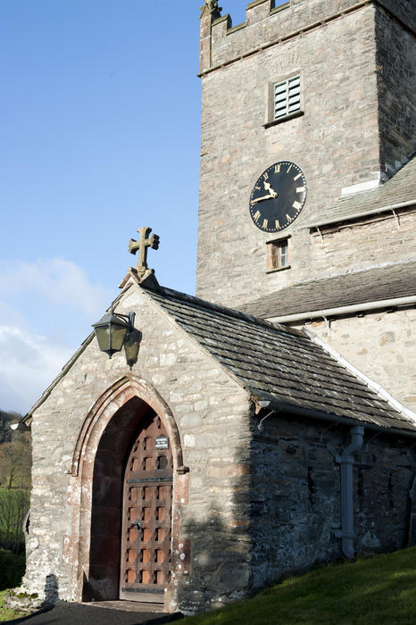 Entrance and clock tower of the historical stone St Michael and All Angel Church in Hawkshead village in the English Lake District, Cumbria and one of the most popular tourist attractions of the area