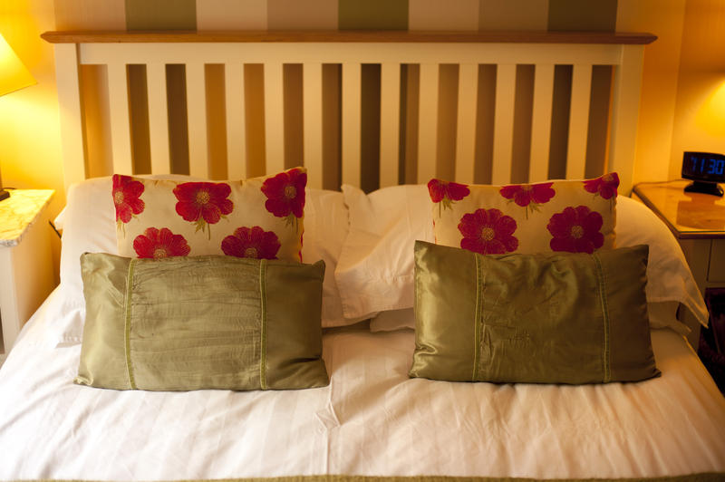 Warmly lit bedroom with two bedside lamps lighting up a comfortable double bed with floral pillows and a slatted wooden headboard