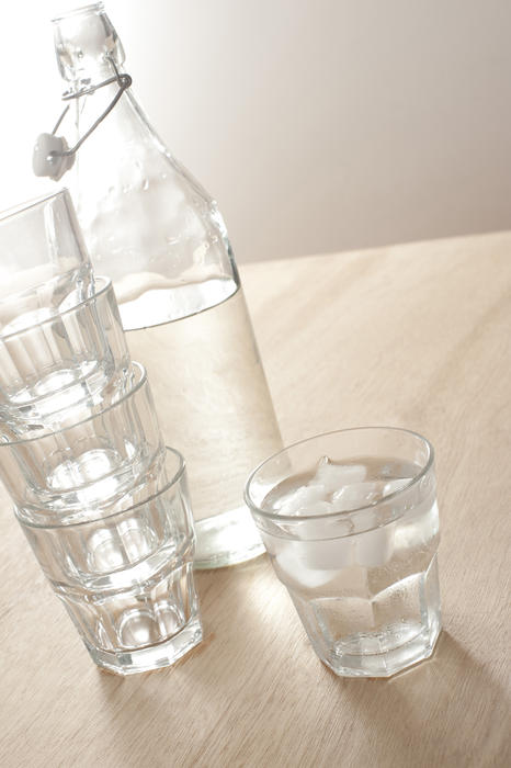 A glass bottle with still water and tumblers on a wooden table