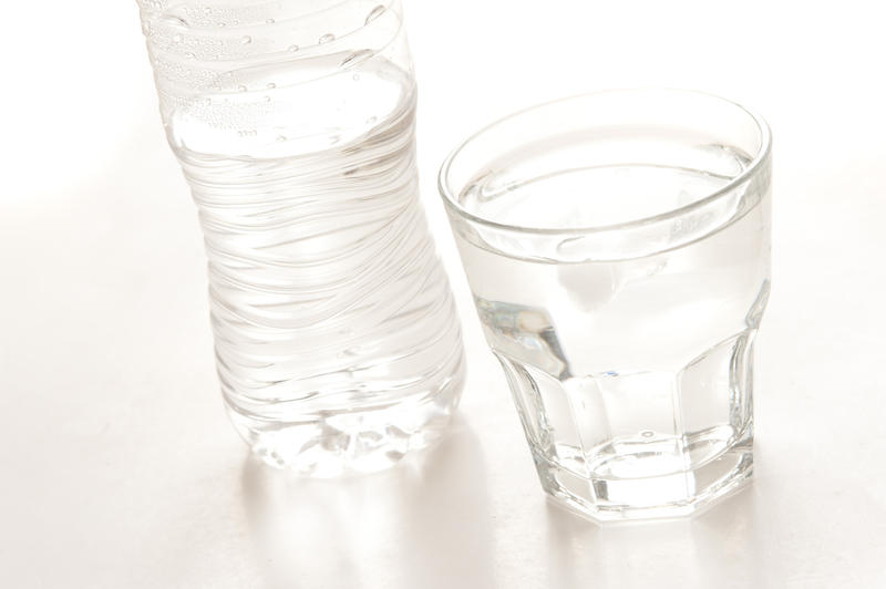 Bottled water in a clear plastic bottle with a full glass alongside on a white background