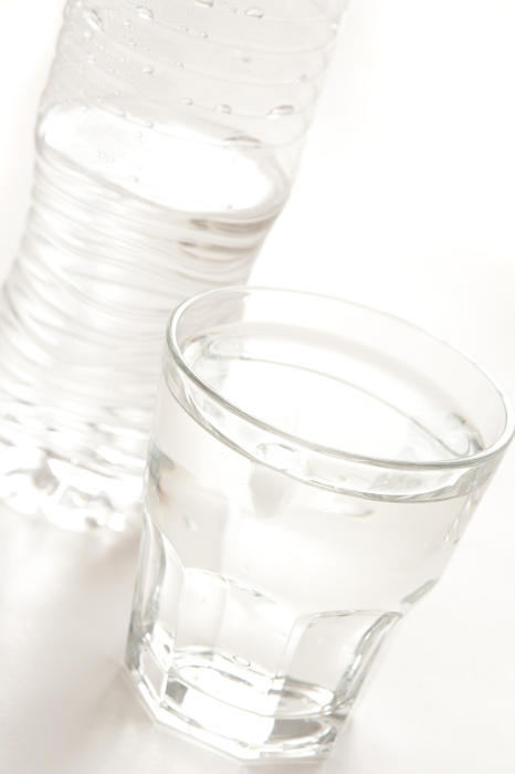Glass of clear clean pure bottled water with the plastic bottle behind on a white background, close up tilted angle