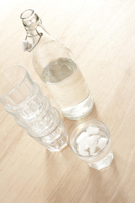 Open bottle of water and several glasses, one with water and ice cubes on wooden table