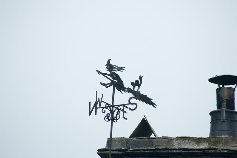 Rooftop weather vane of the silhouette of a wicked witch and her cat riding against a blue sky on a broomstick symbolic of Halloween
