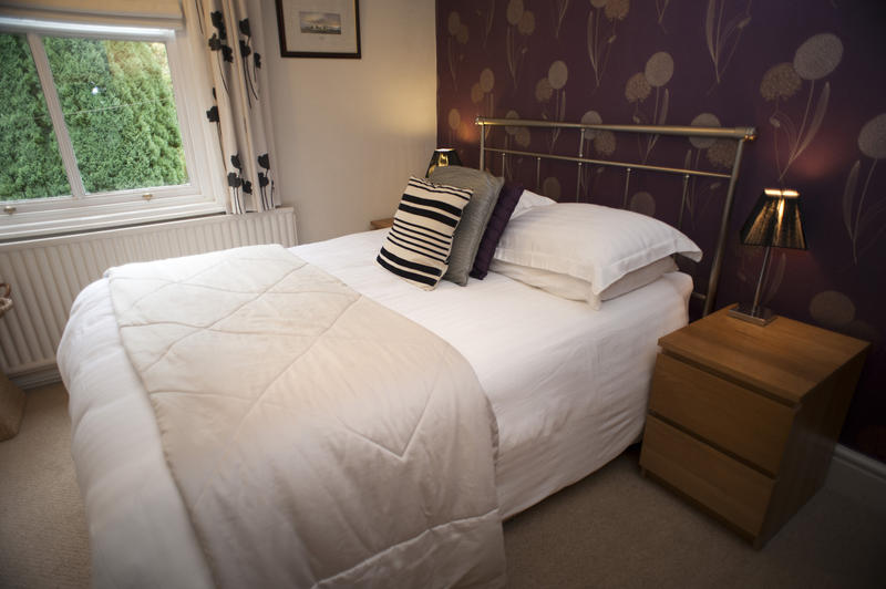 Welcoming bedroom with a classic wrought iron double bed, a quilted throw, neutral decor and a window overlooking greenery in the garden