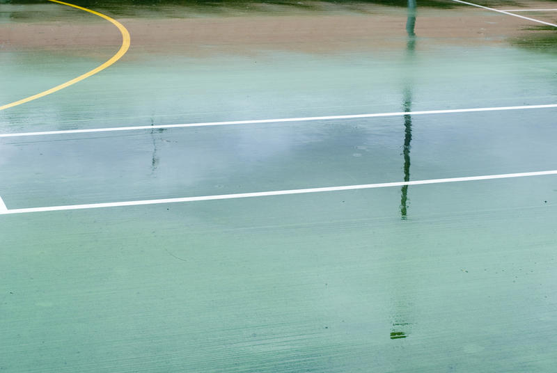 Wet all-weather outdoor sports court with line markings and a yellow circle, background texture view of the deserted court