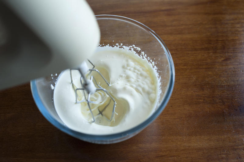 Whipping cream in a glass mixing bowl with a whisk attachment on an electric kitchen mixer, high angle close up view