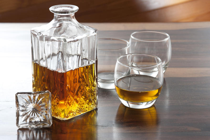 Bottle of whisky and three glasses on wooden table, one filled with alcohol