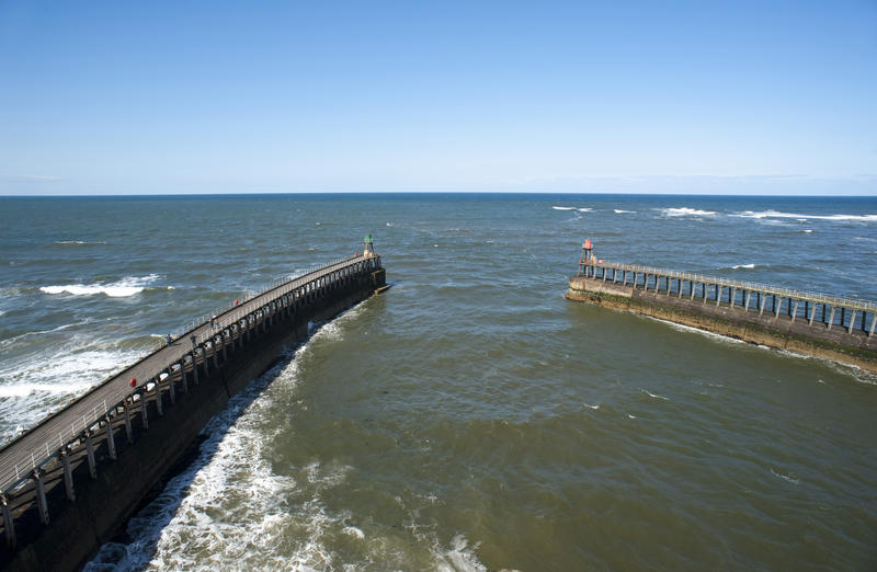 View of Whitby piers and breakwaters from above as they curve towards the harbour entrance and the open sea beyond