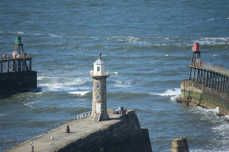 Navigation lights at Whitby harbour with a lighthouse on the end of one pier in the foreground and the two port and starboard beacons on the curving breakwaters