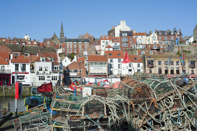 Wire mesh crab traps and lobster pots piled high on the quay at Whitby harbour overlooked by the waterfront houses and the town