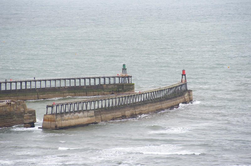 Twin breakwaters at Whitby harbour jutting out into the ocean and topped with coloured beacons to aid in navigation for boats wishing to enter