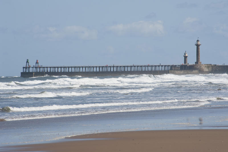 View from the beach across breaking surf of the twin Whitby breakwaters guarding the entrance to the harbour with their guiding beacons