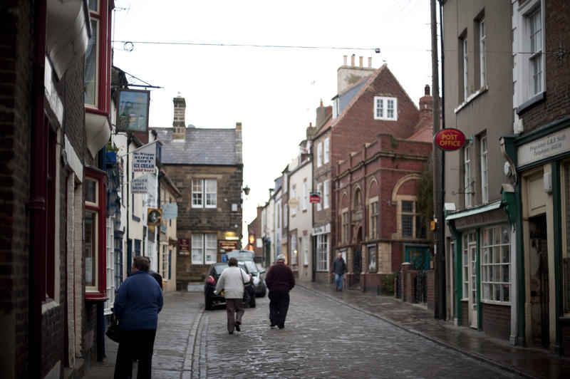 Church street in Whitby with people walking up the narrow cobbled road lined on either side by historical shops and cottages