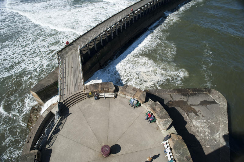 Aerial view of the historical stone West Pier in Whitby and the extended breakwater jutting out into the ocean surf at the entrance to the harbour
